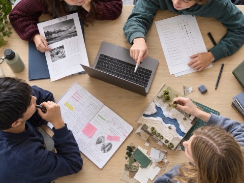 Vier Schülerinnen und Schüler arbeiten mit Laptop, Arbeitsblättern, Notizen und einem Modell – als Darstellung unterschiedlicher Formen des Lernens mit und ohne KI im ISAR-Modell.